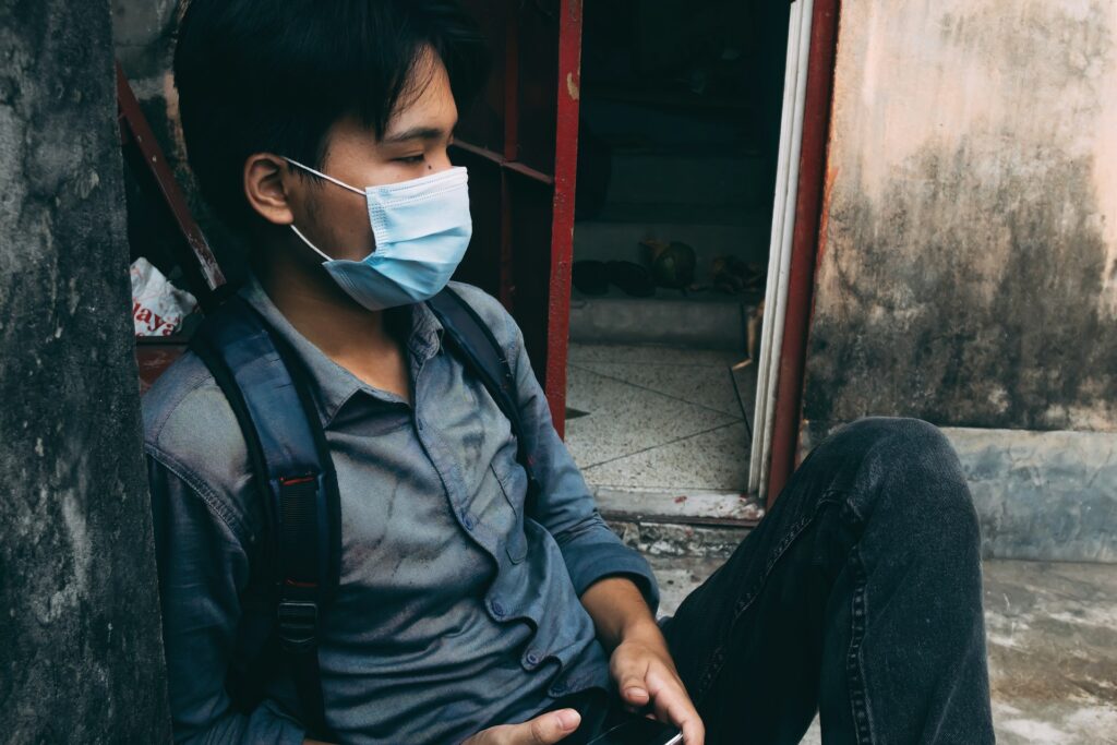 A man sitting on the ground wearing a face mask