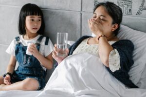 Ill ethnic woman taking medicine while lying in bed near adorable granddaughter