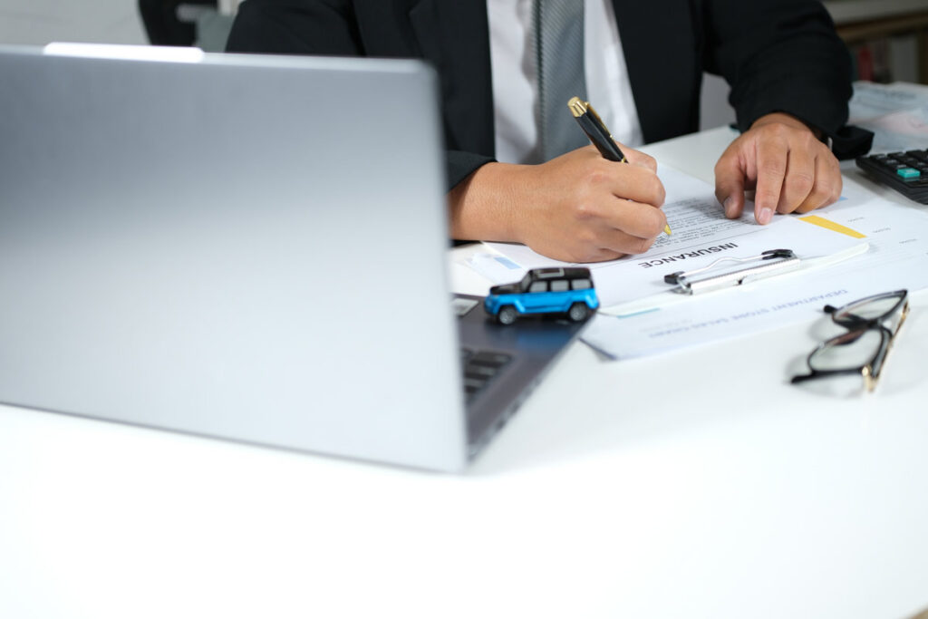 Car purchase and insurance agreement. Signing a car dealership contract. Automotive purchase agreement. Car insurance coverage. Monthly debt burden. Vehicle collateral on a desk in front of a laptop.