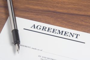 A printed agreement document on a wooden desk with a fountain pen resting on it