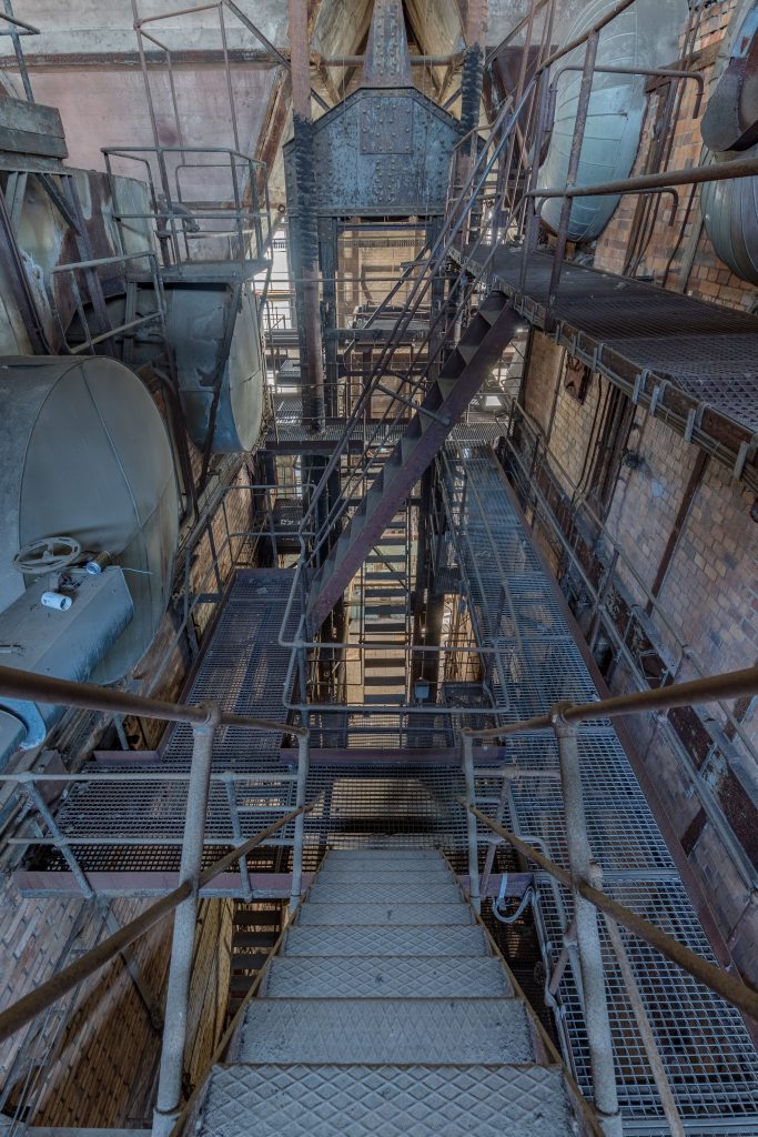 Steel stairways and grated landings climbing several stories inside a coal-fired power plant boiler house, where workers faced asbestos exposure